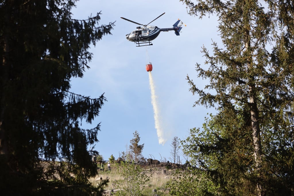 Ein Polizeihubschrauber bringt Wasser zum Löschen an einen Waldbrand bei Stiege im Harz.