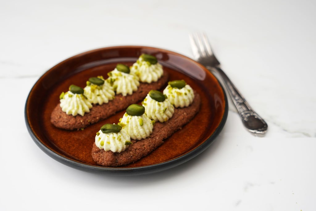 Jeweils vier Spritzer der Mascarpone-Pistaziencrème werden mit einer Spritztülle auf die abgekühlten Gebäckstreifen aufgespritzt.