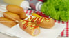 Klassische Corn Dogs bestehen aus aufgespießten Hot-Dog-Würstchen in einer Maisteighülle. Traditionell gibt es Senf und Ketchup dazu.