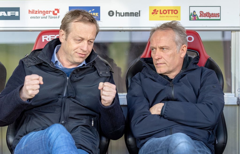 Freiburgs Sportdirektor Klemens Hartenbach (l) und Trainer Christian Streich sitzen auf der Trainerbank.