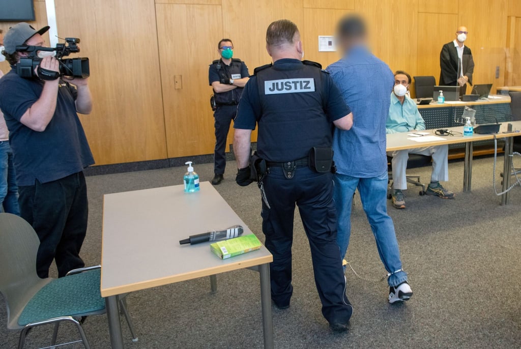 Ein Justizwachtmeister führt den gefesselten Angeklagten (r) ins Gericht.