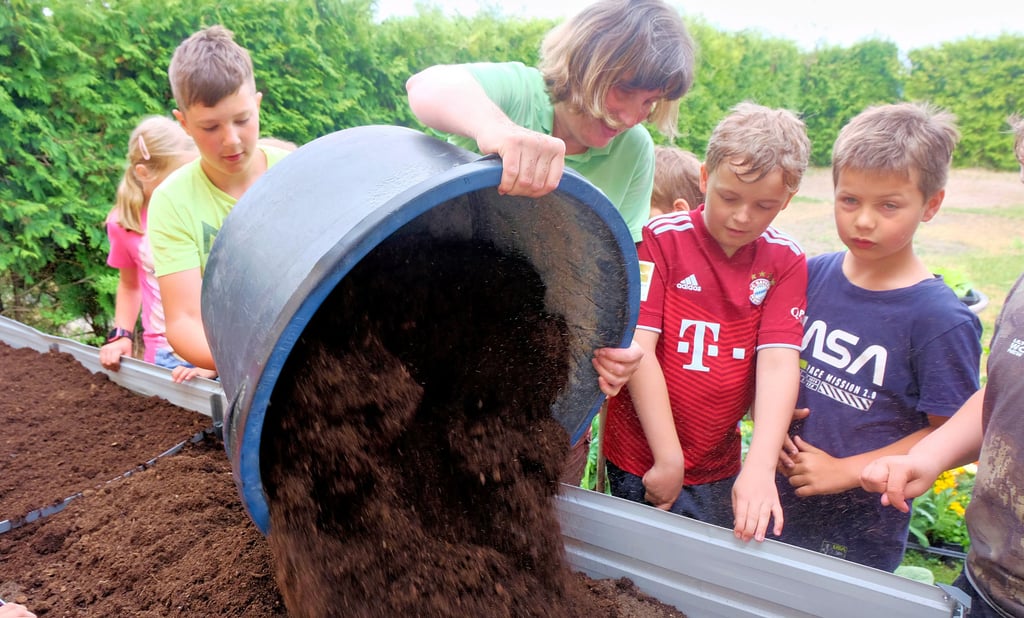 Gartenbaumeisterin Katja Böttcher füllt die Erde in die Hochbeete. Anschließend mischen die Kinder speziellen Dünger unter.
