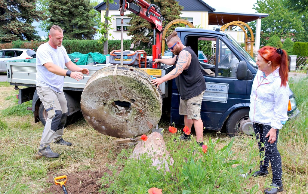 Mitarbeiter einer Steinmetzfirma platzierten den Mühlstein auf einem Findling in „Heinrichsgarten“. Barbara Psoch überwacht die Arbeit.