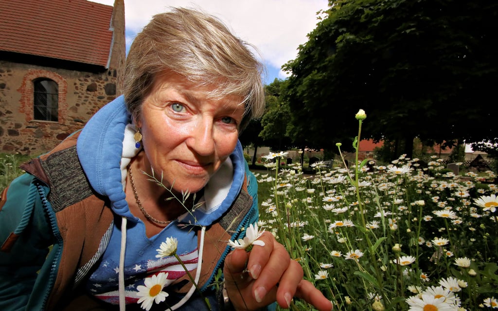 Marietta Klüdtke riecht an einer Magerite. Die anspruchslosen Blumen stehen hier auf einer Wiese. Viele Stunden in der Woche kümmert sie sich ehrenamtlich mit Erika Prawitz um den Garten rund um die Kirche. In den vergangenen Jahren hat sich das Gelände stark verändert.