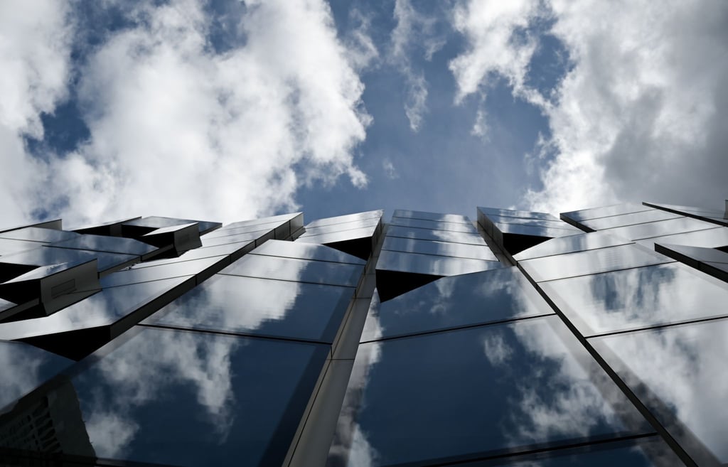 Weiße Wolken und blauer Himmel spiegeln sich in der Glasfassade des Gebäudes der DWS Group.