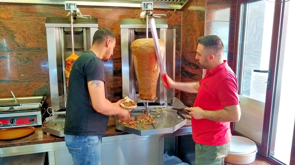 Deniz-Grill-Chef Murat Kara schneidet mit seinem Dönermesser  das Fleisch vom Spieß, wärend sein Mitarbeiter das Brot befüllt. 