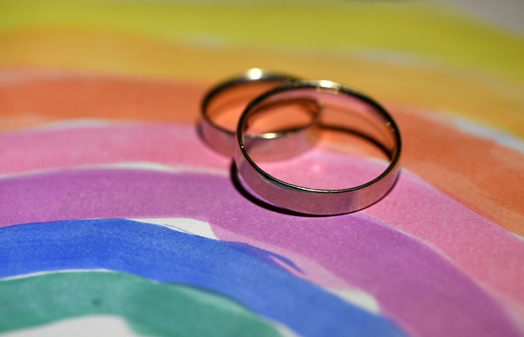 Zwei Eheringe liegen auf einer gemalten Regenbogenfahne .