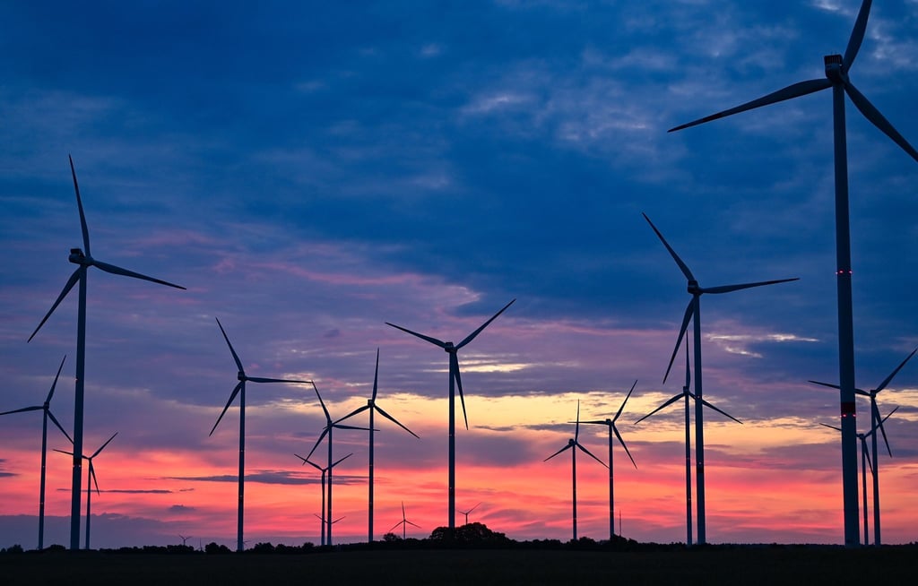 Goldene Stunde In Brandenburg: Kurz vor dem Sonnenaufgang drehen sich die Rotorblätter von Windenergieanlagen im Wind.