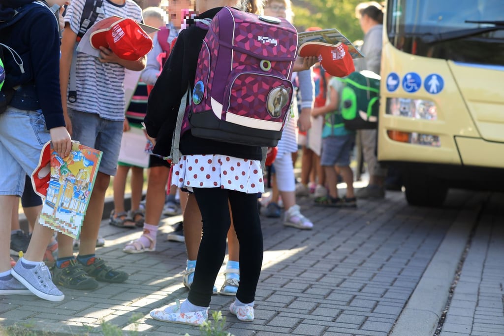 Kinder stehen mit ihrem Ranzen vor einem Schulbus. In manchen Bundesländern sorgt das 9-Euro-Ticket jetzt für Rückforderungen vom Amt.