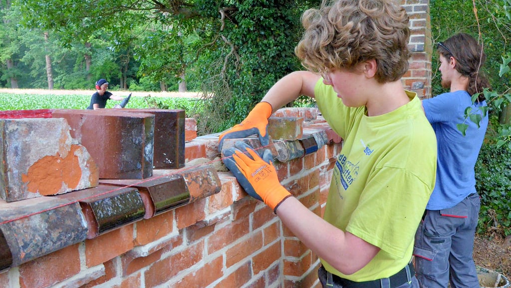 Lea Lehnert (links) aus Dresden hilft dabei, die Mauer der Kirche in Vollenschier schick zu machen. Mit ihr waren 17 weitere junge Leute nach Vollenschier gereist, die ein Freiwilliges Soziales Jahr im Denkmalschutz absolvieren.