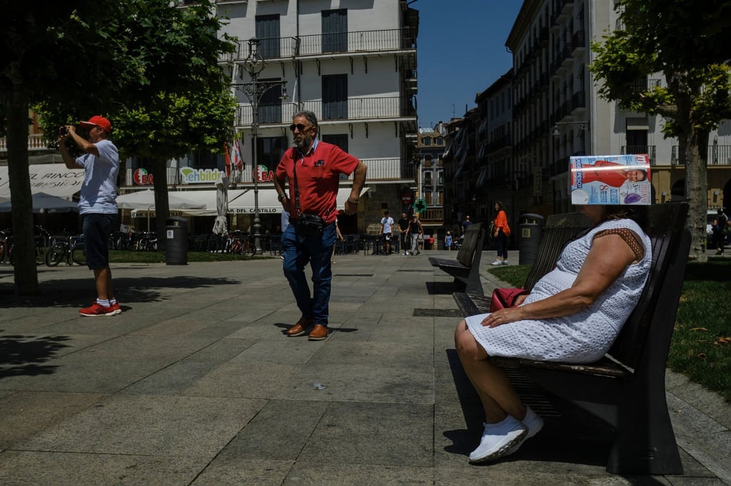 Eine Frau schützt sich in Pamplona mit einer Zeitschrift.