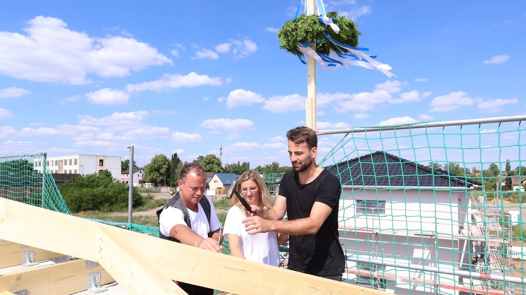 Blau-weißer Himmel, blau-weiße Richtkrone: Fußballer Christian Beck und Ehefrau Paulin feiern Richtfest. Sie bauen in Magdeburg ein Eigenheim. Dachdeckermeister Michael Grothe hilft und hält den Nagel fest.