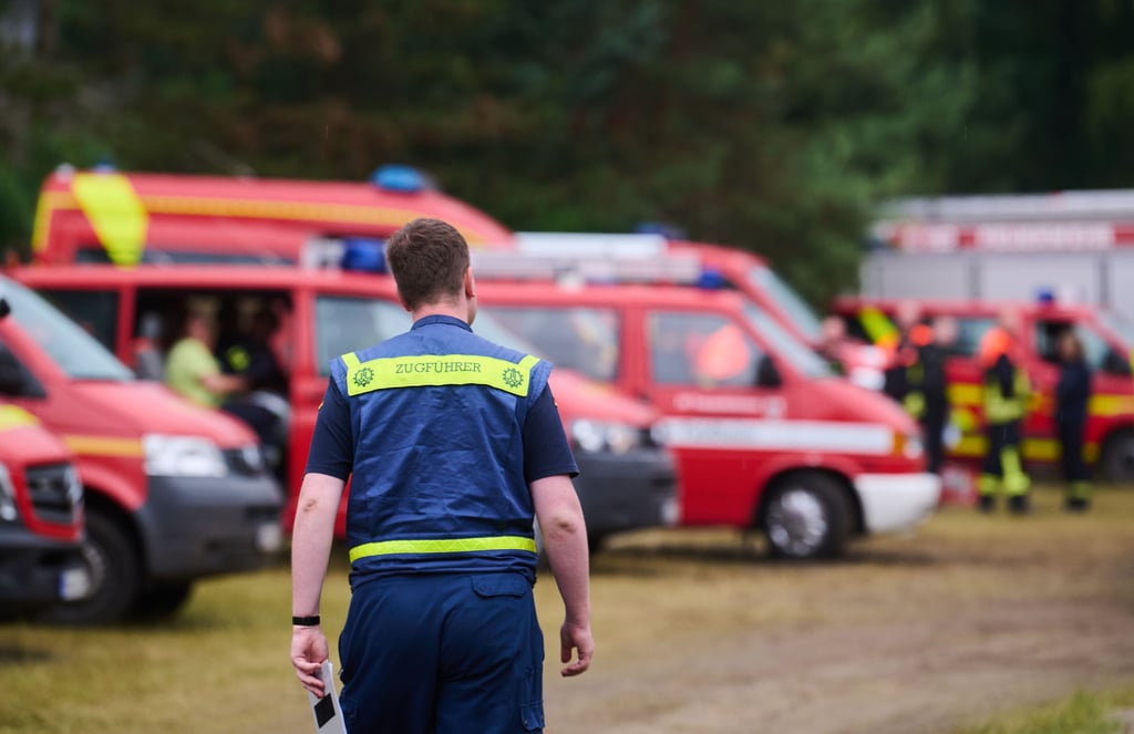 "Zugführer" steht auf dem Rücken einer Einsatzkraft, der auf dem Bereitstellungsraum für Feuerwehr, THW und Polizei nahe Treuenbrietzen aufgebaut wurde. Starker Regen hat im Kampf gegen zwei große Waldbrände in Brandenburg am frühen Montagmorgen für Entlastung gesorgt. Zunächst brannten nachts noch 135 Hektar Waldflächen bei Treuenbrietzen - 80 Kilometer südwestlich von Berlin, wie Behördenvertreter vor Ort berichteten.