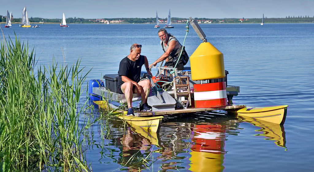 Ralf Meyer und Frank Kleeblatt transportieren die neue Boje mit dem Boot zu ihrem Platz in der Goitzsche.