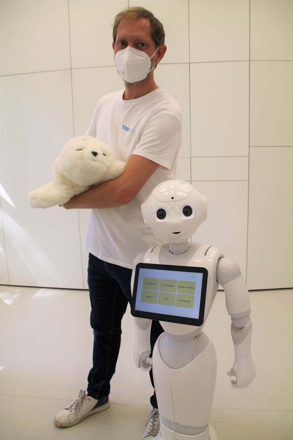 Sieht aus wie ein Plüschtier, doch TDG-Koordinator Karsten Schwarz hölt einen Emotionsroboter im Arm. Der Roboter neben ihm heißt Pepper.