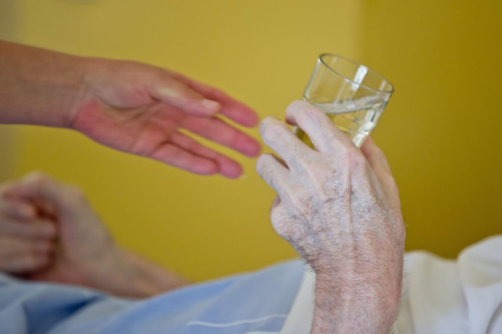 Eine Krankenpflegerin reicht einem Patienten ein Glas Wasser.