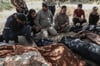 Trauernde sitzen 2021 neben eingehüllten Leichen unter Bäumen in Idlib und warten darauf, dass Kampfflugzeuge abziehen.