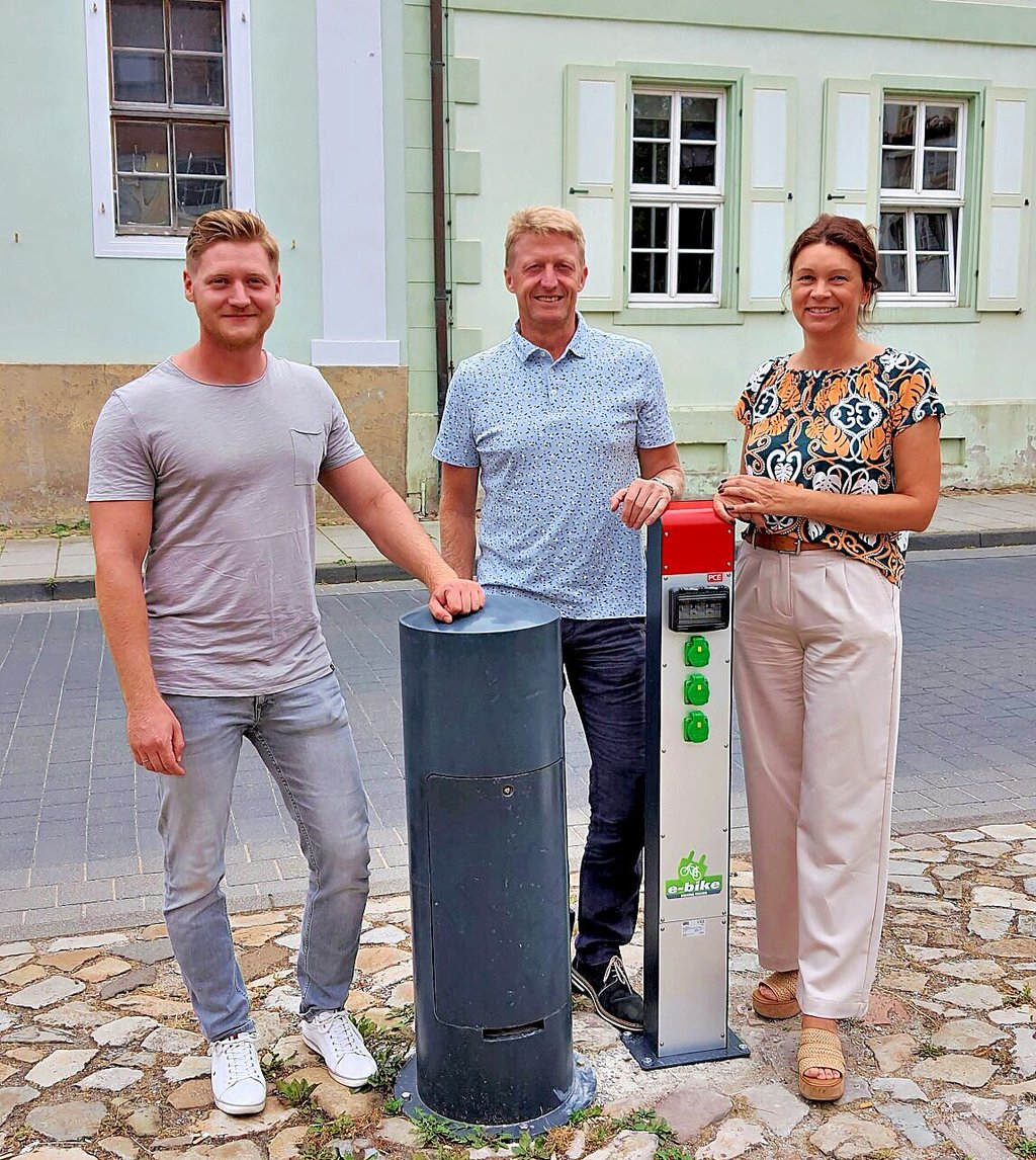 Jost Mattisseck, Vorsitzender Heimatverein „Grafschaft Barby“ (v.l.), Torsten Reinharz, Bürgermeister der Einheitsgemeinde und Antje Klimek, Kommunalreferentin avacon, an der neuen Ladesäule auf dem Marktplatz.