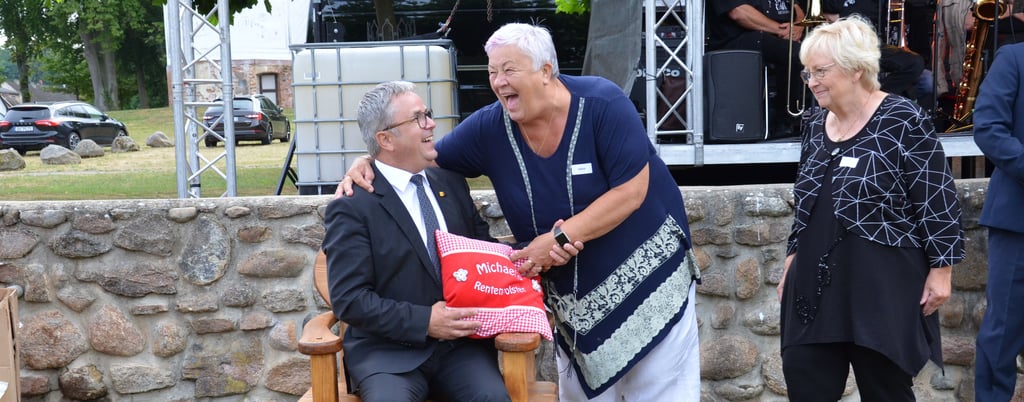 Die Vorsitzende des Bildungsausschusses beim Altmarkkreis Salzwedel, Angelika Scholz (Linke, Bildmitte) verabschiedet sich gemeinsam mit der Vorsitzenden der Linksfraktion im Kreistag, Gabriele Gruner, herzlich vom scheidenden Landrat Michael Ziche, dem die Kreistagsfraktion der Linken einen Holzstuhl und ein Kissen mit der humorvollen Aufschrift "Michaels Rentenpolster" geschenkt hat.