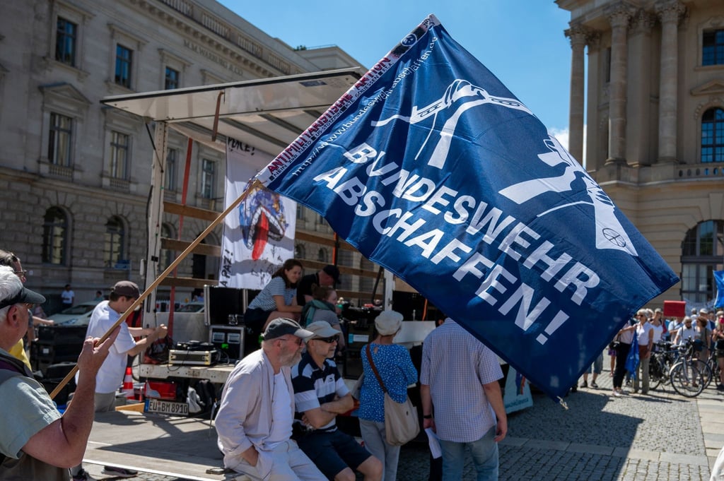 Ein Teilnehmer hält bei einer Demonstration auf dem Bebelplatz eine Flagge mit der Aufschrift „Bundeswehr abschaffen!“.