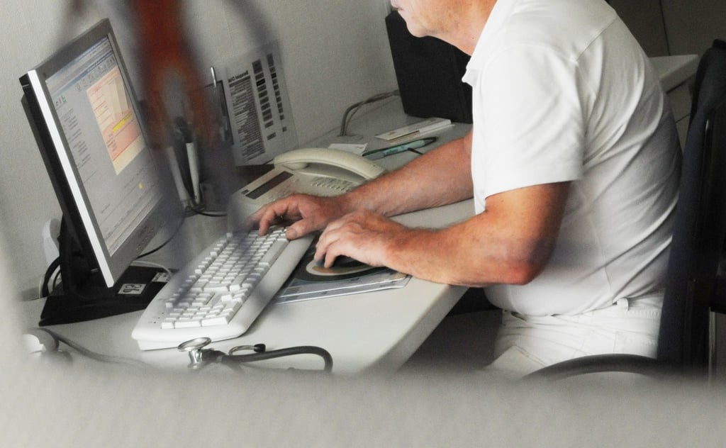 Ein Arzt sitzt in seiner Praxis an einem Computer.