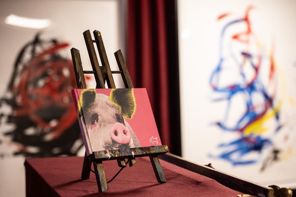 Ein Buch mit dem Konterfei in der Ausstellung des malenden Schweins "pigcasso" vor Werken.