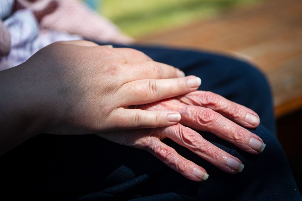 Die Hand einer Pflegefachkraft liegt auf der Hand einer Bewohnerin des Pflegeheims.