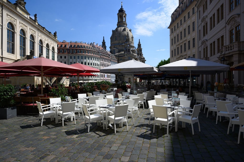 Stühle, Tische und Sonnenschirme eines Restaurants stehen auf dem Neumarkt vor der Frauenkirche.
