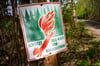 Ein Schild mit der Aufschrift „Schütz den Wald vor Brandgefahr“ hängt in einem Wald an einem Waldweg.