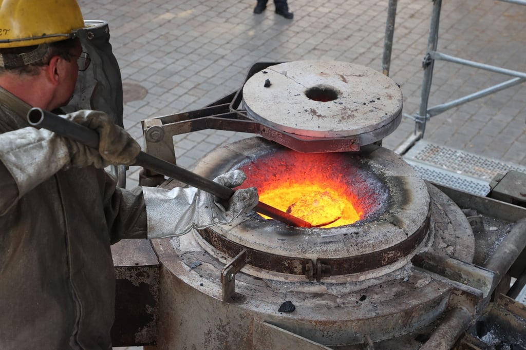 Mitarbeiter einer Glockenbaufirma arbeiten an einem Ofen, in welchem Metall erhitzt wird und dann über einen Steg in flüssiger Form in die Hülle der neuen Glocke gegossen wird.