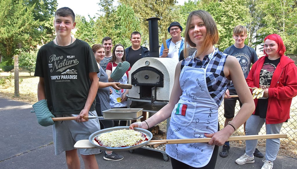 Gina Broß (vorn) und Neo Märkisch (l.)schieben bei der Einweihung die erste Pizza in den Backofen. Beim Backofen-Projekt dabei sind auch Justine Stief (hinten; v.l.), Tom Scholkmann, Nimea Brestrich, Tristan Wendt, Lukas Weber, Brain Wilke und Celine Kranz.