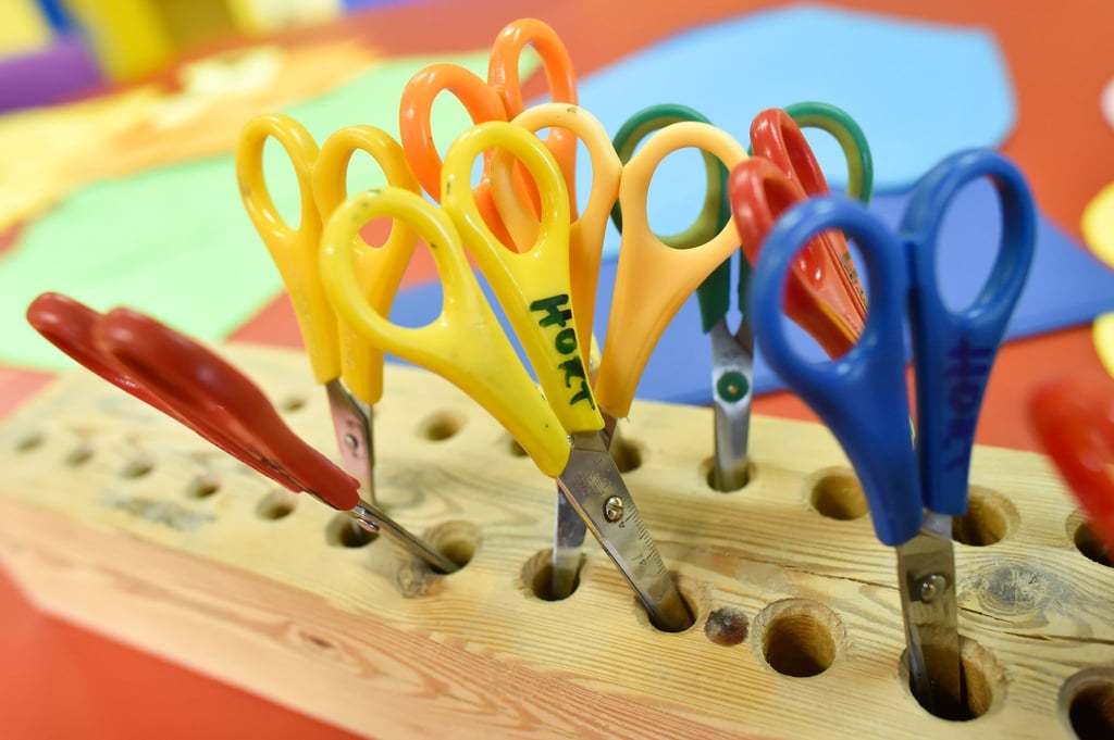 „Hort“ steht auf einer Kinderschere, die zusammen mit weiteren Scheren in einem Holzblock steckt.