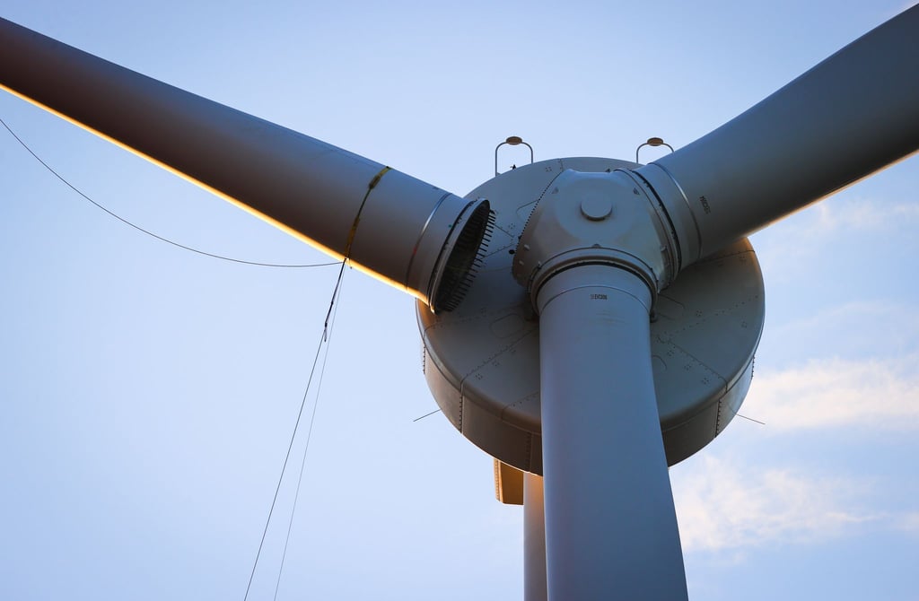 Mit einem mobilen Kran wird das dritte Rotorblatt an einer Windkraftanlage von Enercon montiert.