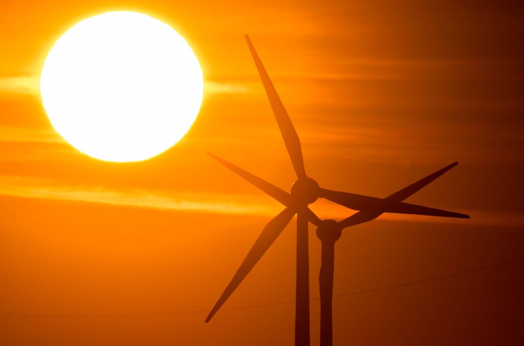 Die Sonne geht hinter Windrädern auf.