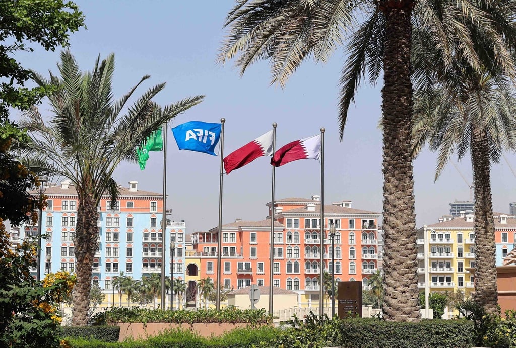 Flaggen in den Farben Katars und eine Fifa-Flagge sind hinter Palmen zu sehen.