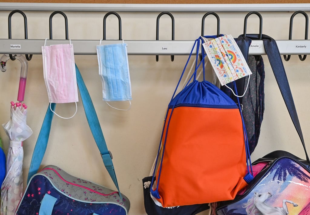 Medizinische Masken und Schultaschen hängen in einer Schulgarderobe.