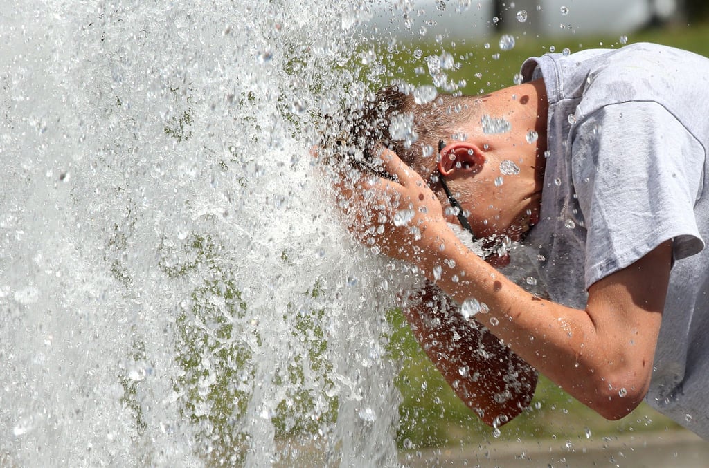 Ein Mann erfrischt sich an einem heißen Sommertag im Berliner Lustgarten an einem Brunnen.