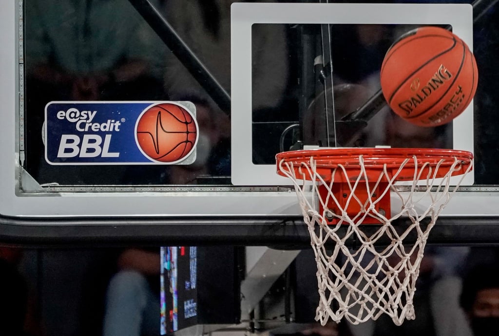 Ein Ball fliegt auf den Korb zu, an dem ein Logo der Basketball-Bundesliga klebt.