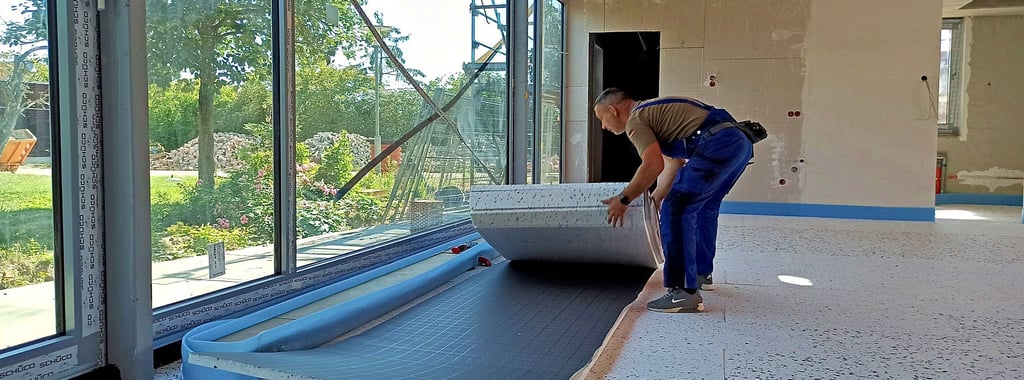 Ein Handwerker legt die Dämmung für die Fußbodenheizung aus. Darauf werden im nächsten Schritt die Rohe für die Heizung verlegt.