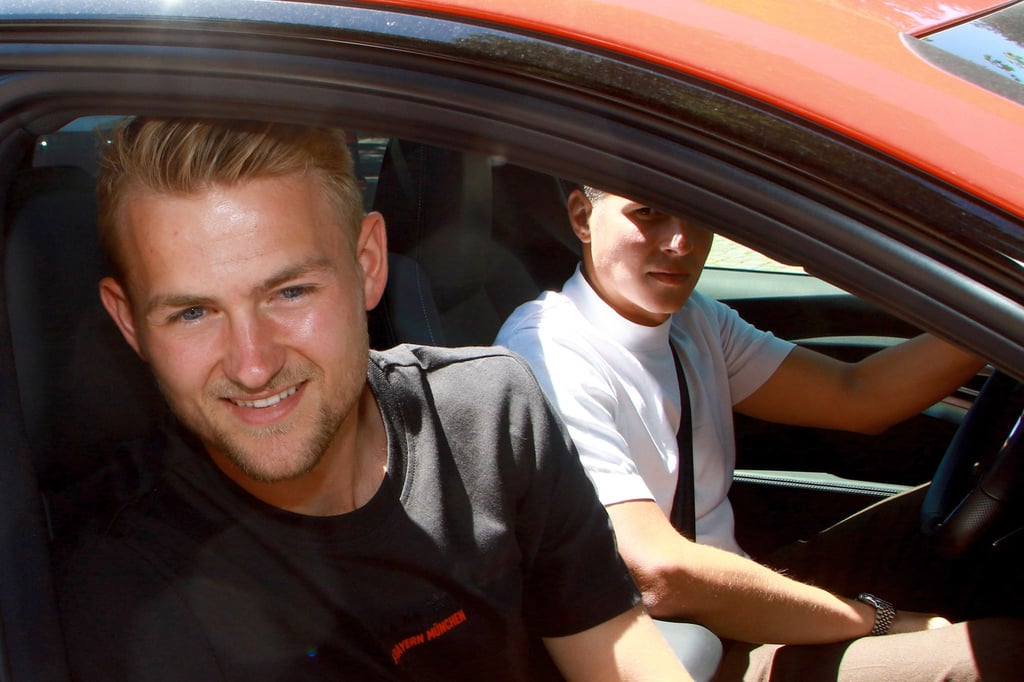Matthijs de Ligt (l) lächelt beim Verlassen der Bayern-Geschäftsstelle aus dem Fenster eines Autos.