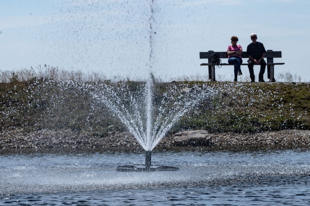 Touristen sitzen auf einer Bank hinter einem Springbrunnen auf dem Wurmberg im Harz.