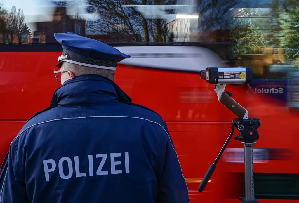 Ein Polizeioberkommissar steht mit einer Laserpistole vor einer Schule und misst die Geschwindigkeit.