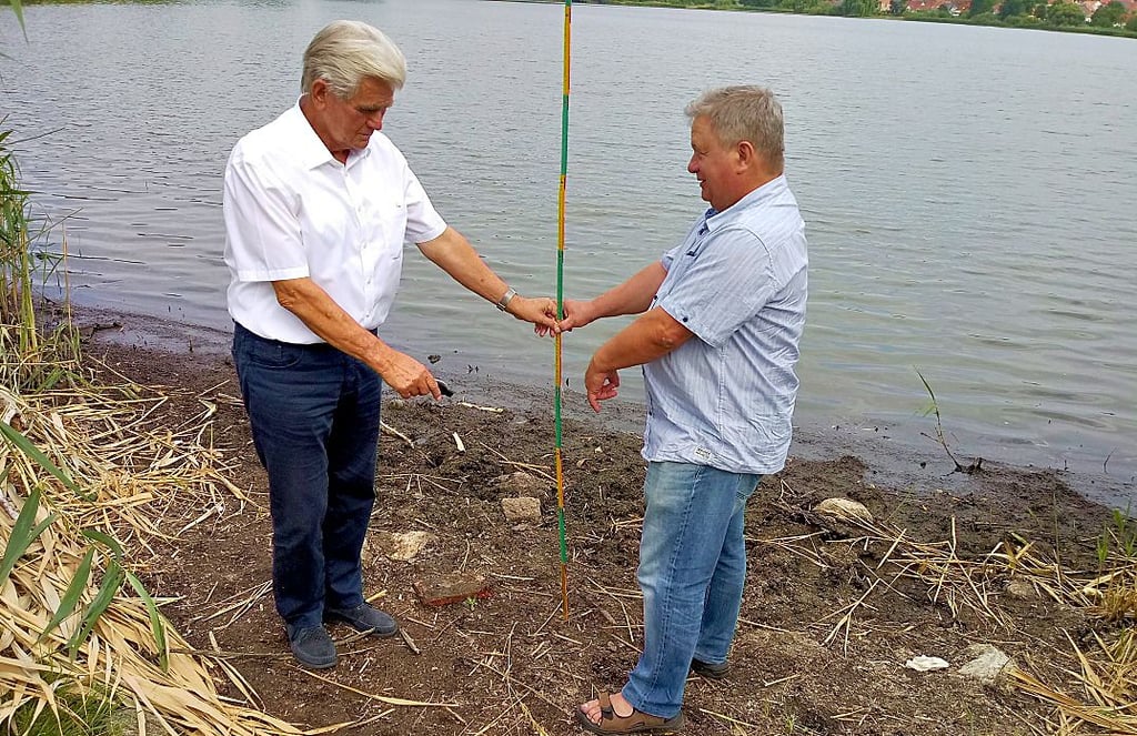Eckhard Jockisch und Hans Sill messen am Rand des Sees den Rückgang des Wasserspiegels.