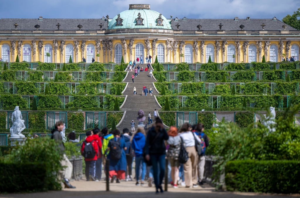Zahlreiche Besucher spazieren bei sonnigem Wetter im Park Sanssouci auf das Schloss zu.