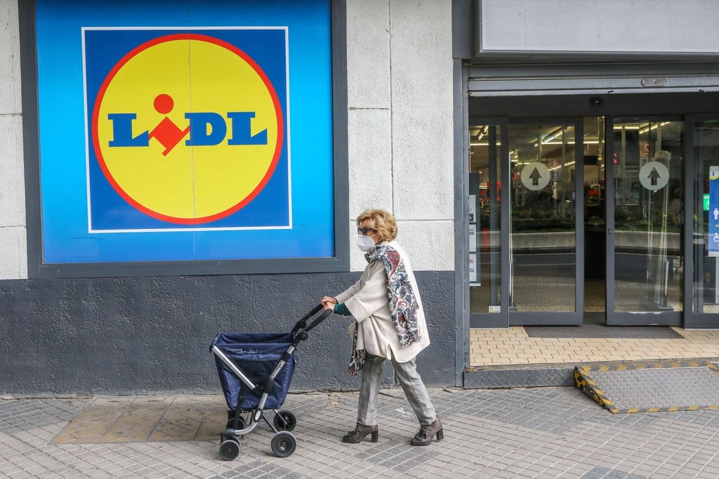 Eine Frau mit Rollator trägt einen Mund-Nasen-Schutz und passiert ein Einkaufsladen.