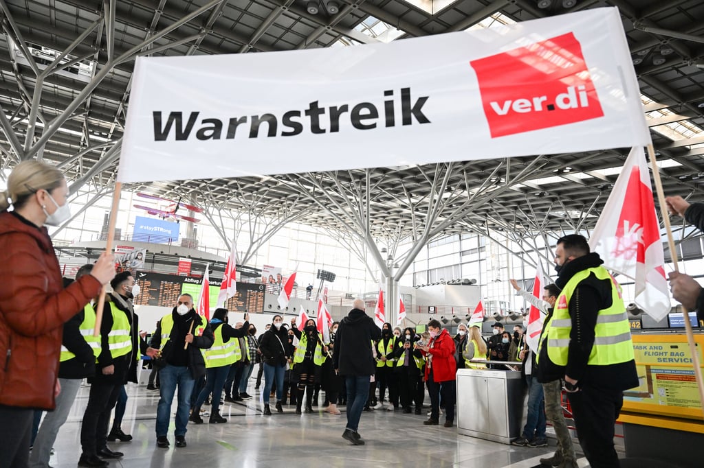 Mitglieder der Gewerkschaft Verdi stehen mit Fahnen und Transparenten bei einem ganztätgigen Warnstreik in einer Halle des Flughafens Stuttgart. Am Mittwoch drohen erneut Flugausfälle