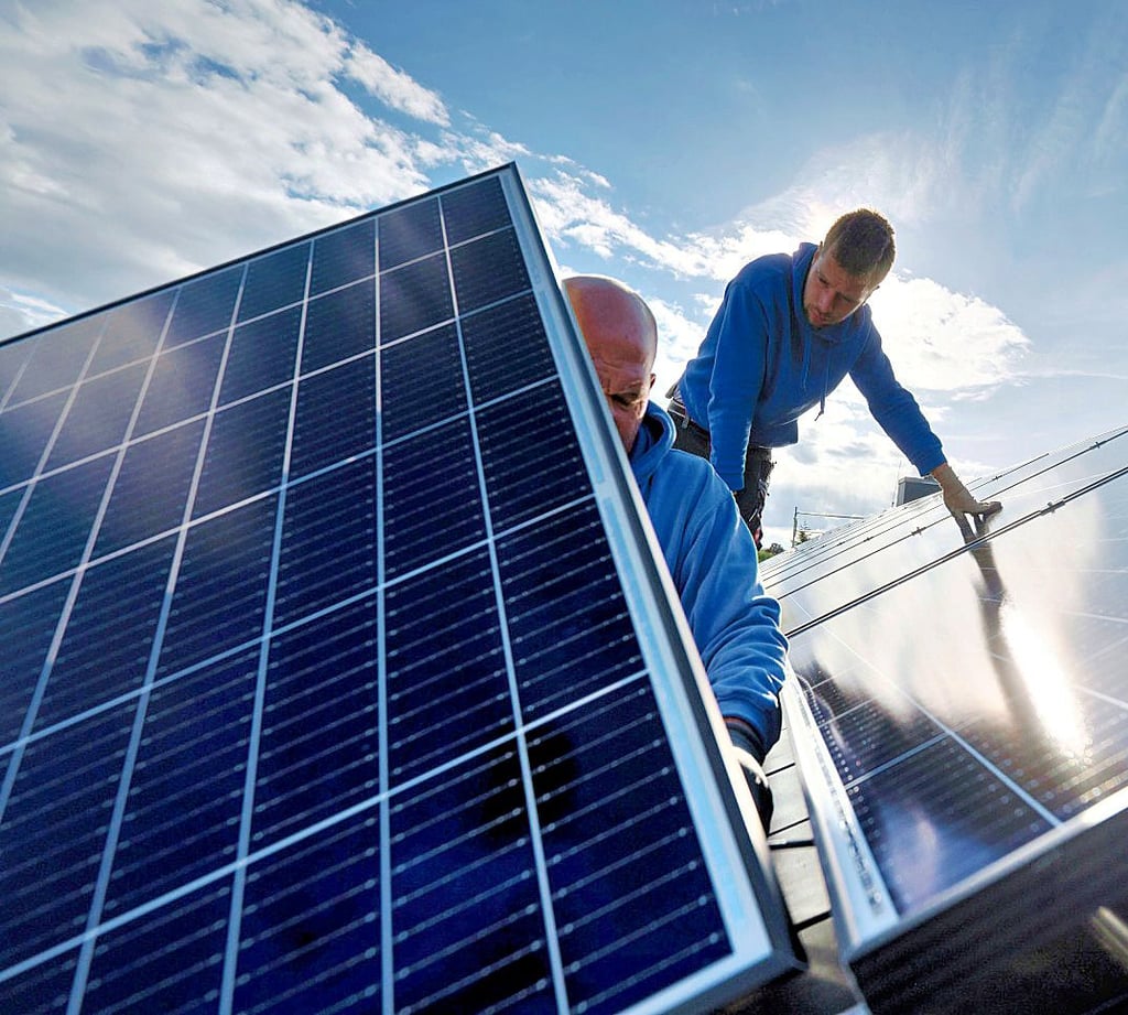 Mitarbeiter einer Spezialfirma installieren Photovoltaikmodule auf dem Dach eines Wohnhauses.