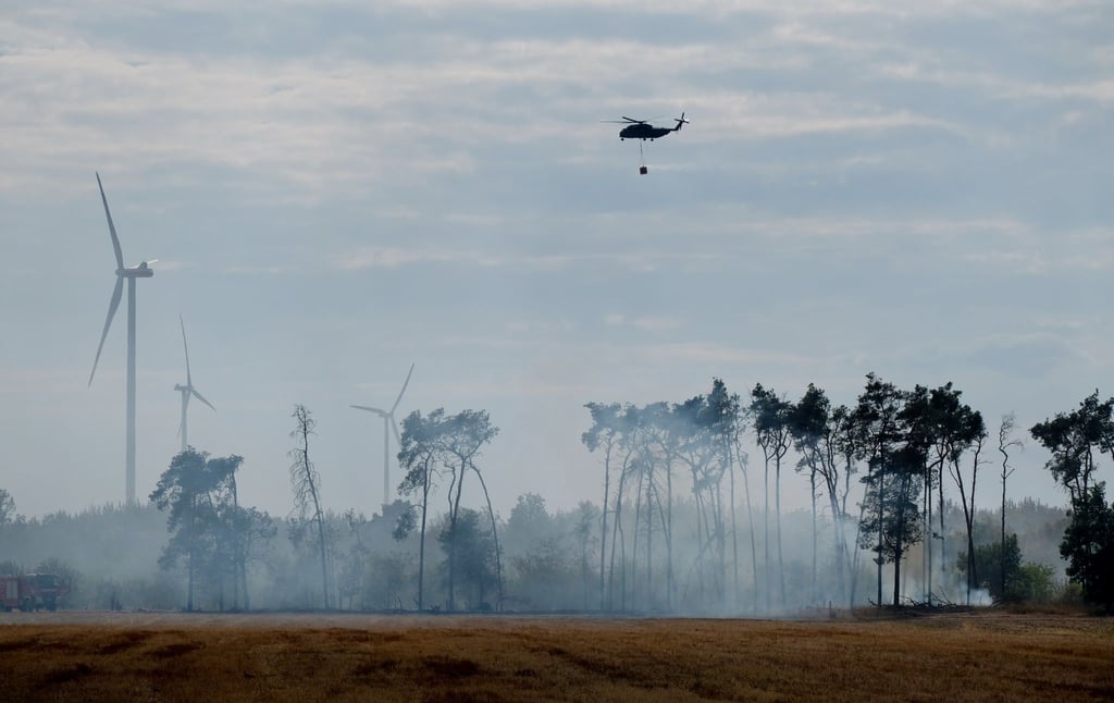 Ein Hubschrauber mit Wasserbehälter fliegt über einen Waldbrand im Landkreis Elbe-Elster.