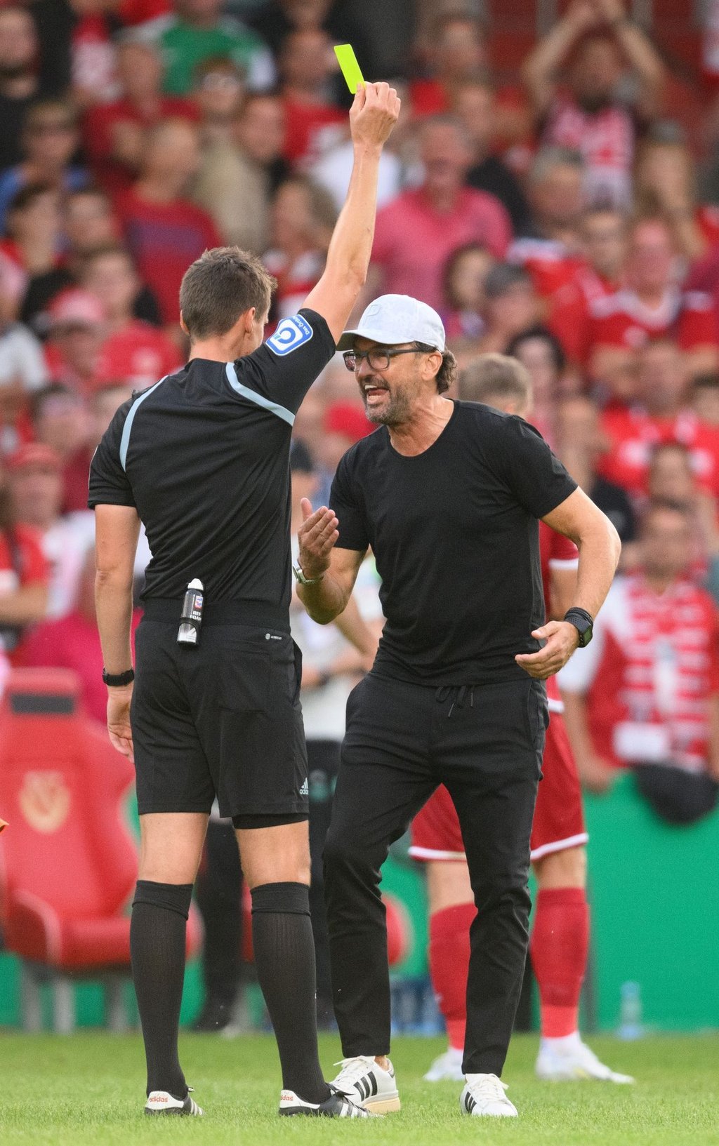Claus-Dieter „Pele“ Wollitz diskutiert nach dem Spiel mit Schiedsrichter Daniel Siebert und bekommt die Gelbe Karte gezeigt.