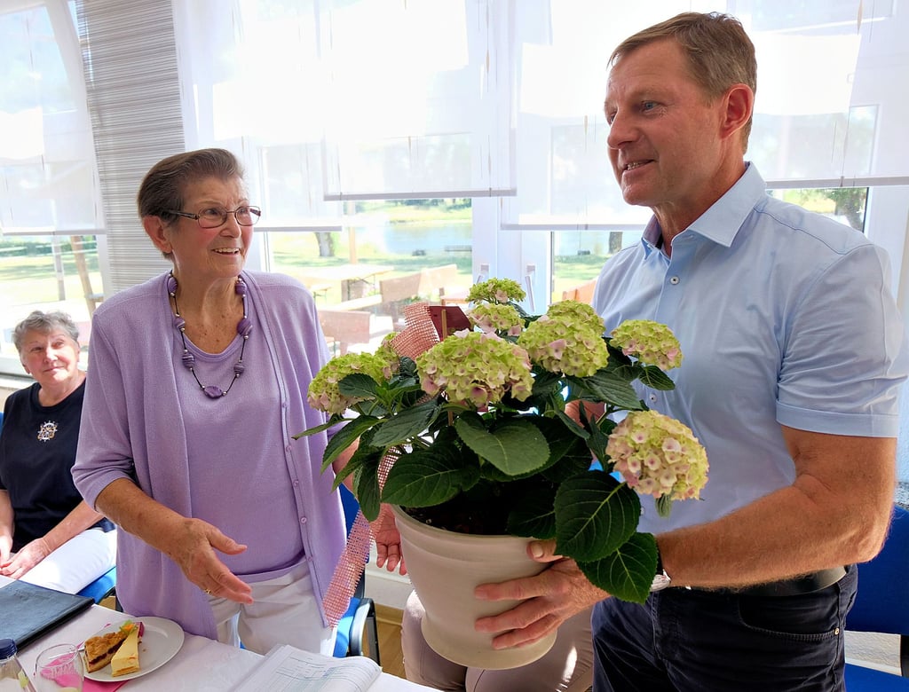 Bürgermeister Peter Müller überreicht Margitta Müller im Bootshaus von Elster eine Hortensie.